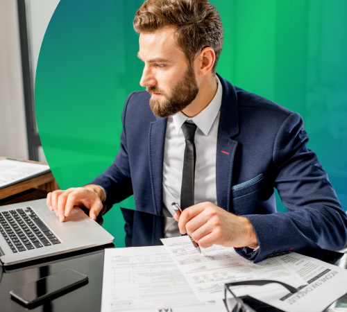 A man in a suit sat at a desk with a laptop reviewing documents